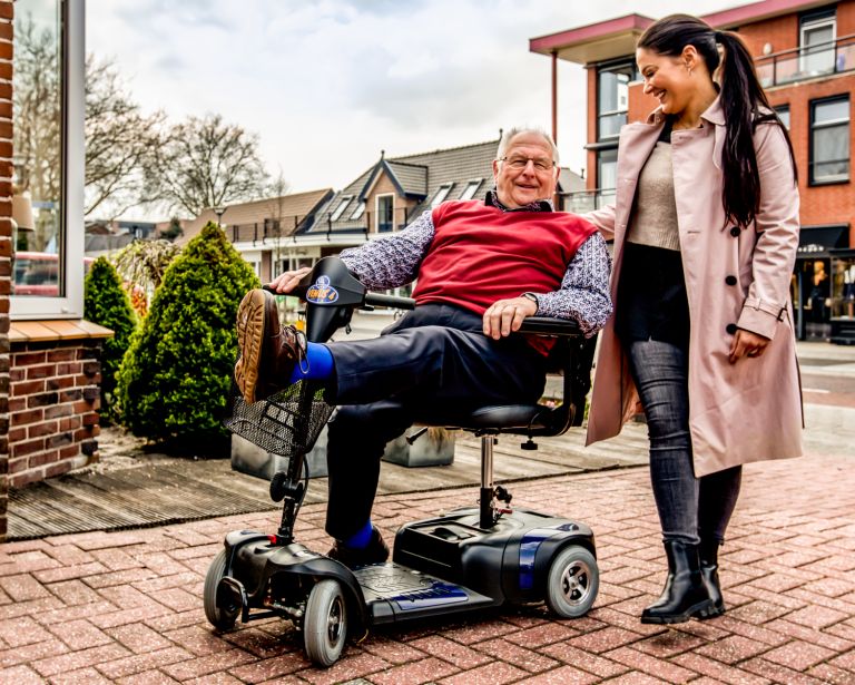 Lachende-zorgverlener-begeleidt-zorgvrager-in-scootmobiel